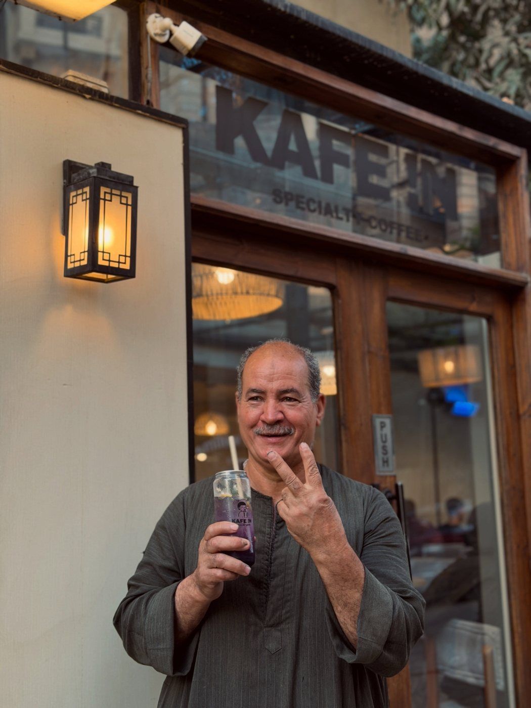 A smiling guest with a drink in front of the walnut doors and brass lanterns