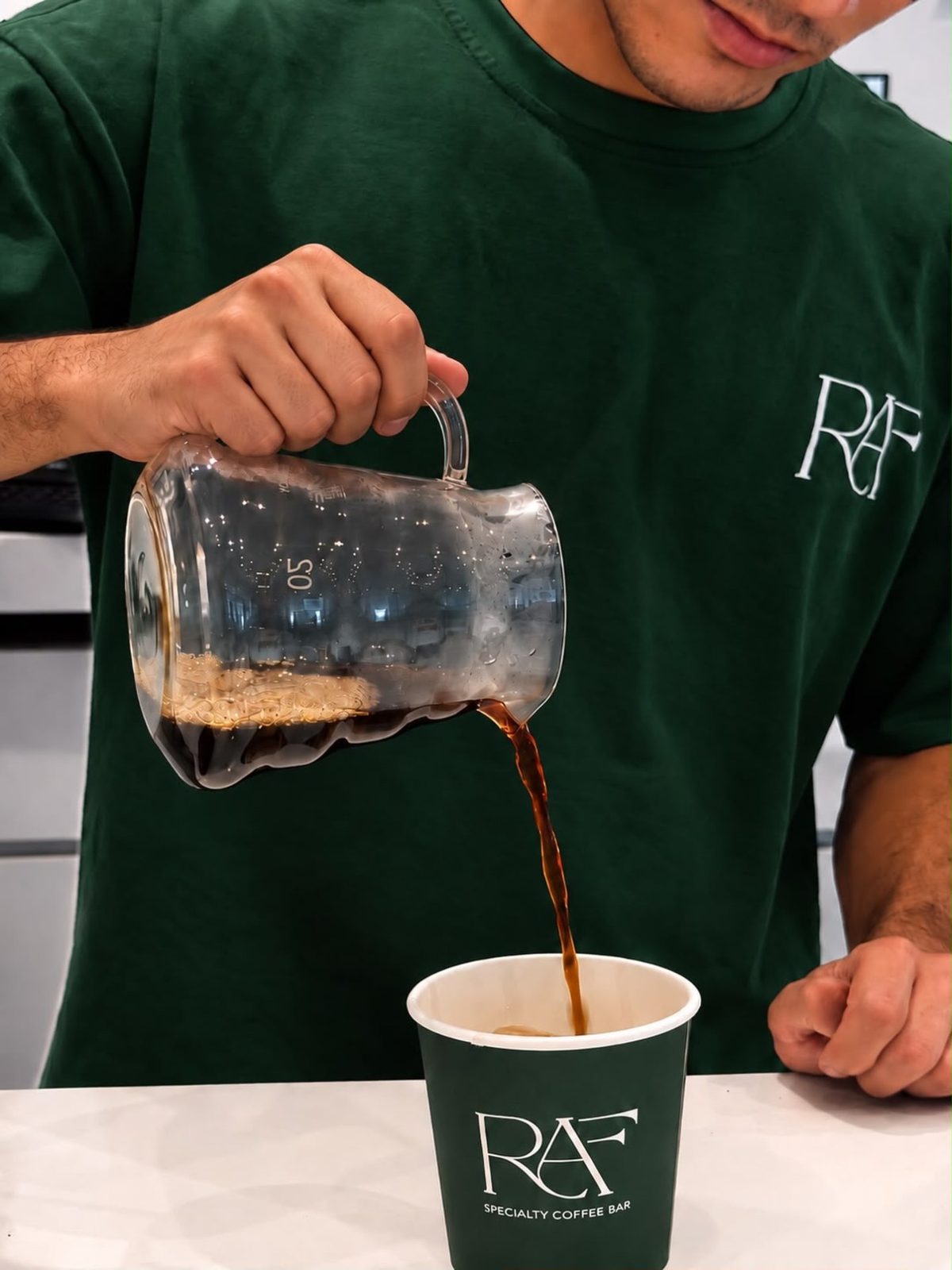 A barista in a green RAF t-shirt pouring filter coffee into a green RAF cup